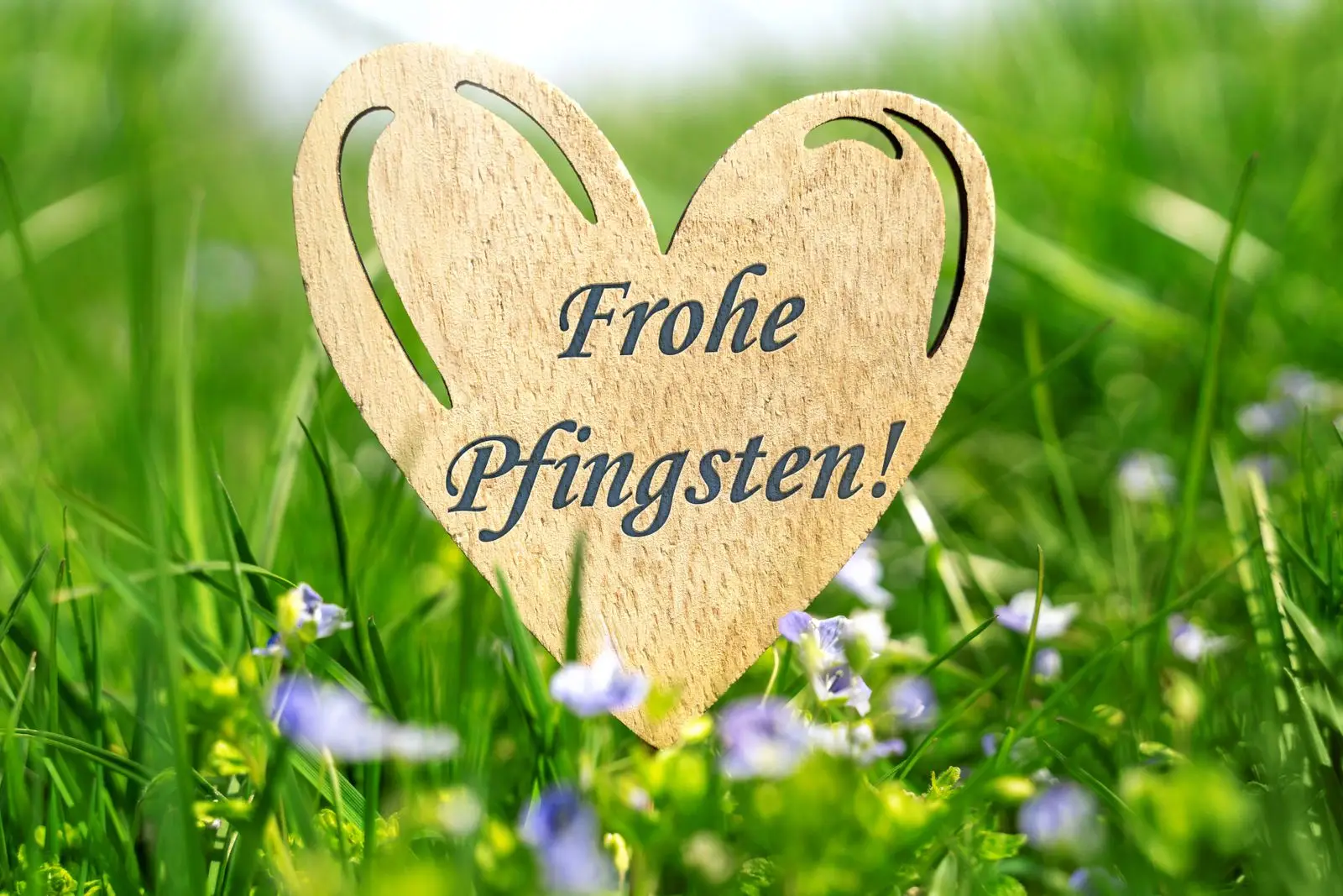 Frohe pfingsten mit graviertem holzherz im gras