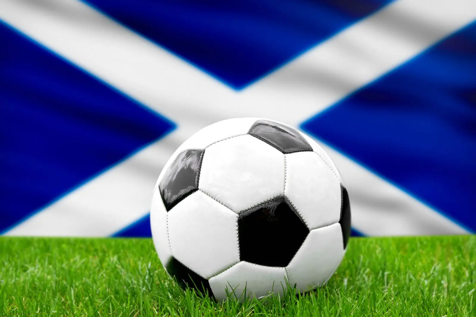 Ein fußball vor der schottischen fahne symbolisiert die nationalmannschaft von schottland im fußball.
