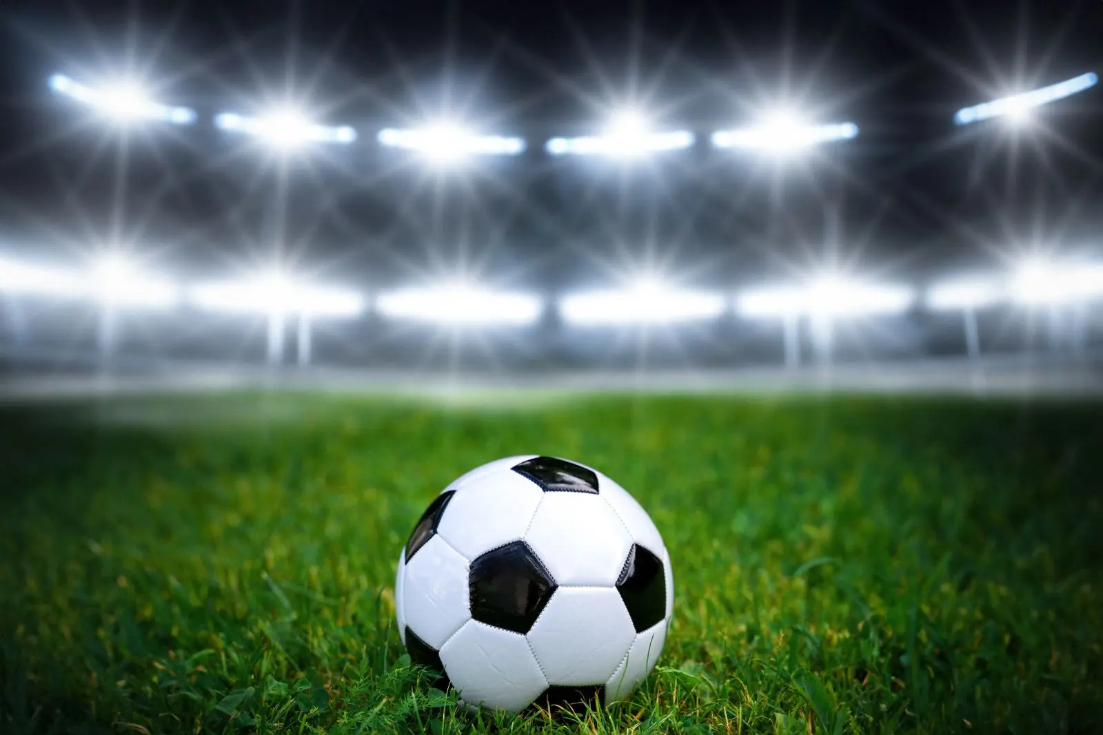 Fußball auf grünem rasen in einem beleuchteten stadion während eines fußballspiels, umgeben von hellen flutlichtern.