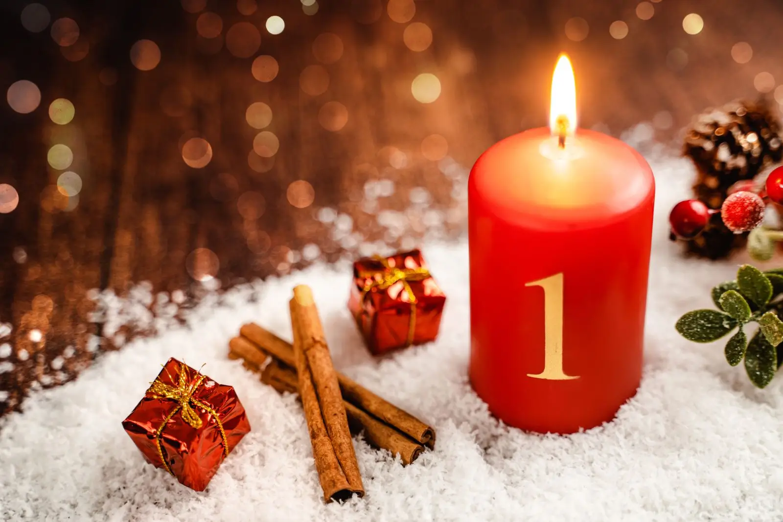 Rote kerze mit der zahl 1, zimtstangen und geschenken im schnee als adventsgruß zum ersten advent.
