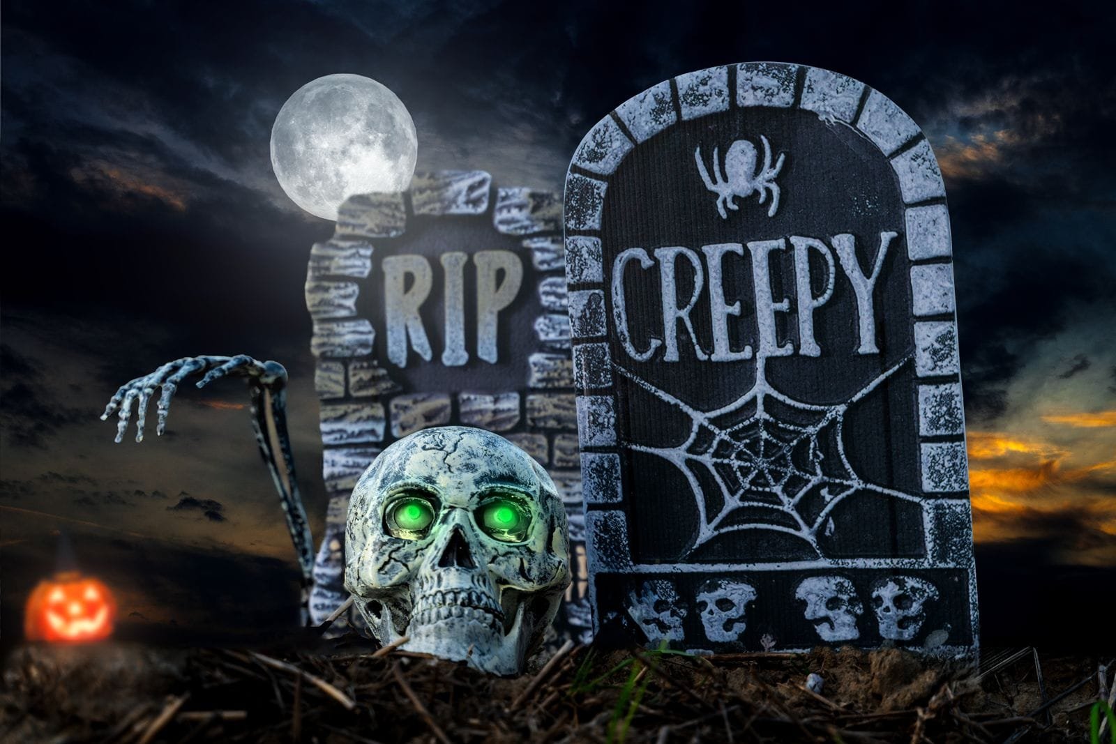 Halloween-szene mit zwei grabsteinen, einem leuchtenden totenschädel mit grünen augen und einem kürbis im hintergrund. Einer der grabsteine trägt die aufschrift ‚rip‘, der andere ‚creepy‘ mit einem spinnennetz und einer spinne. Der vollmond leuchtet am düsteren nachthimmel.