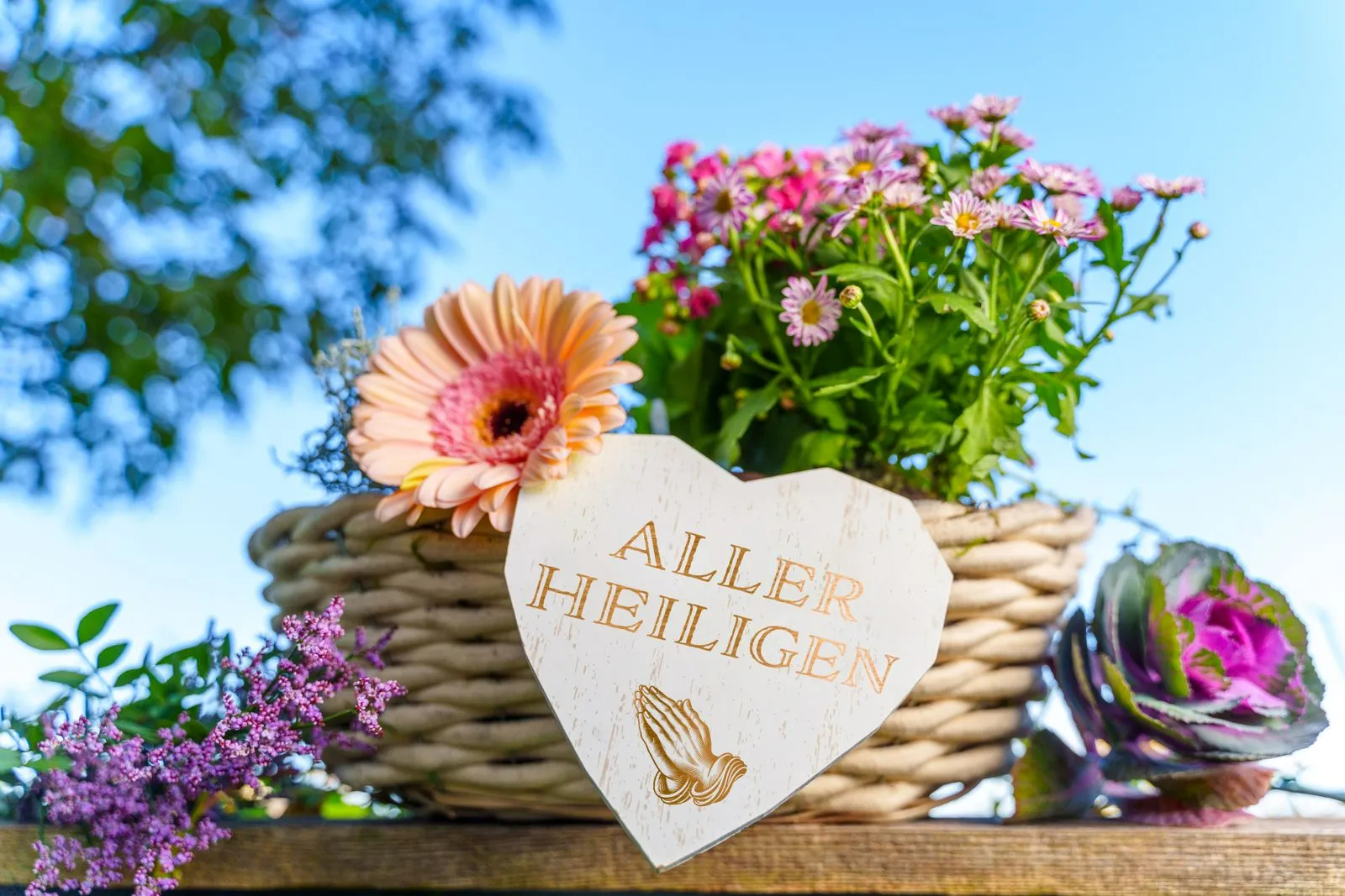 Ein liebevoll gestaltetes grabgesteck zu allerheiligen mit blumen und einem herzschild mit der aufschrift ‚allerheiligen‘. Das bild symbolisiert den feiertag im herbst, an dem verstorbene geehrt und ihrer gedacht wird.