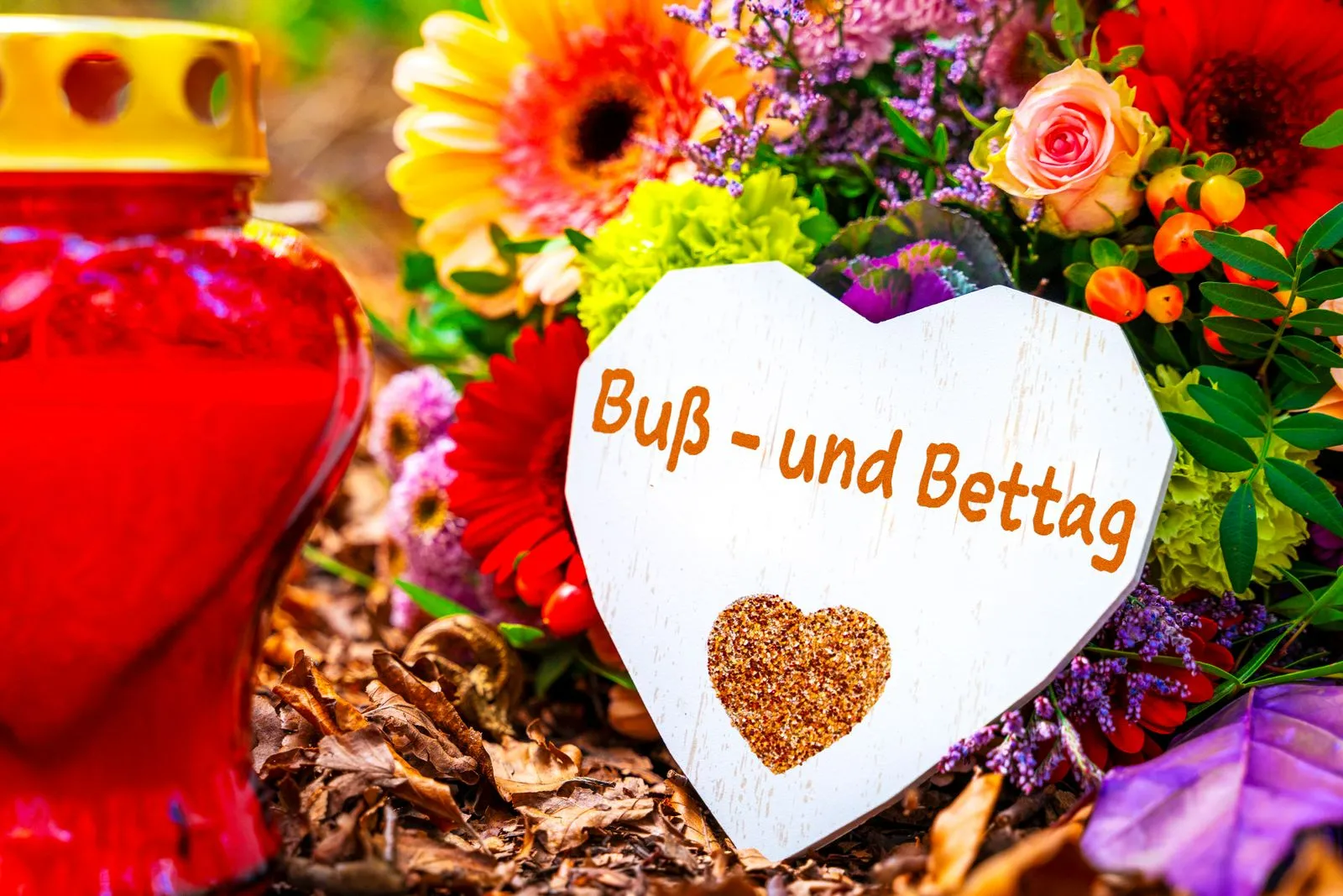 Buß- und bettag steht auf einem herz, neben roten grabkerze und bunten blumen, symbolisch für den evangelischen feiertag.