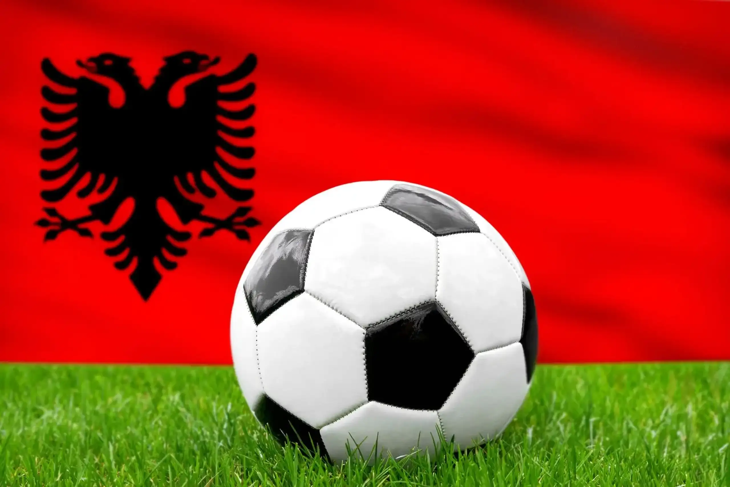 Albanien fußball nationalmannschaft mit fußball vor albanischer flagge auf grünem rasen