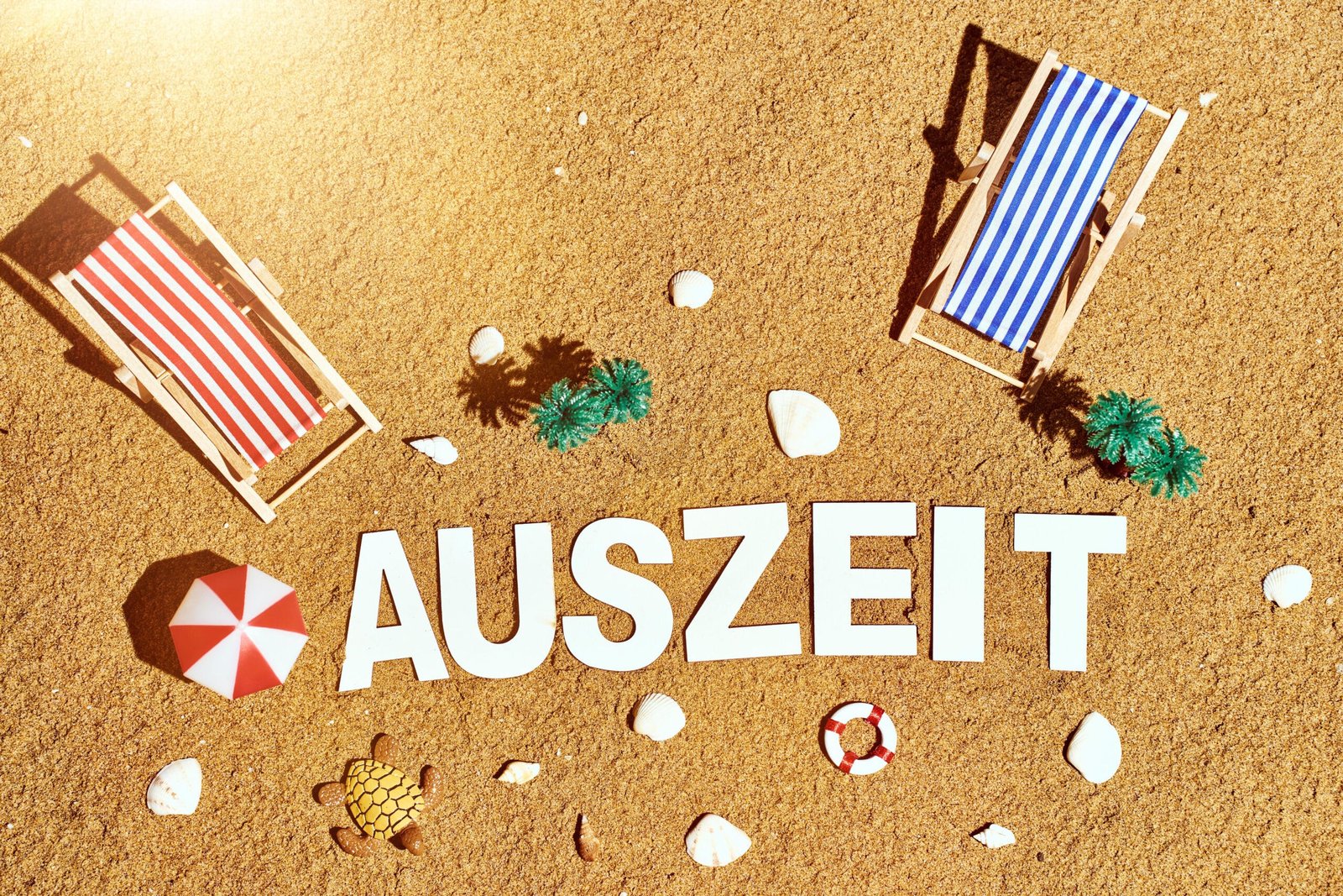 Schriftzug: auszeit, im sand am strand mit sonnenliegen