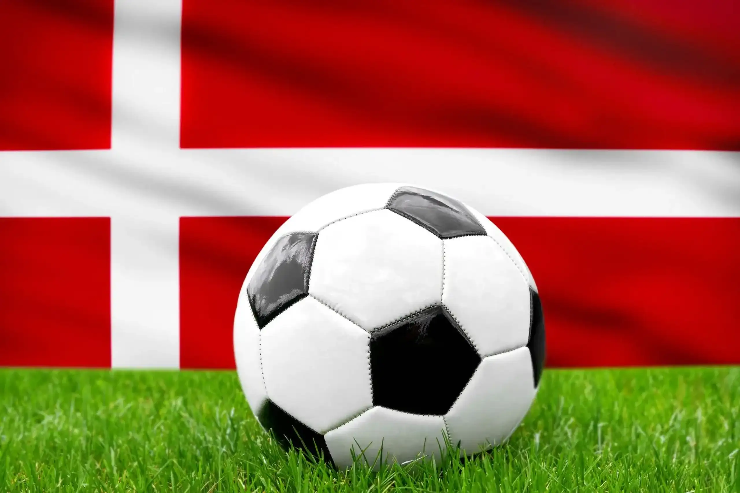 Dänemark fußball nationalmannschaft mit fußball vor dänischer flagge auf grünem rasen