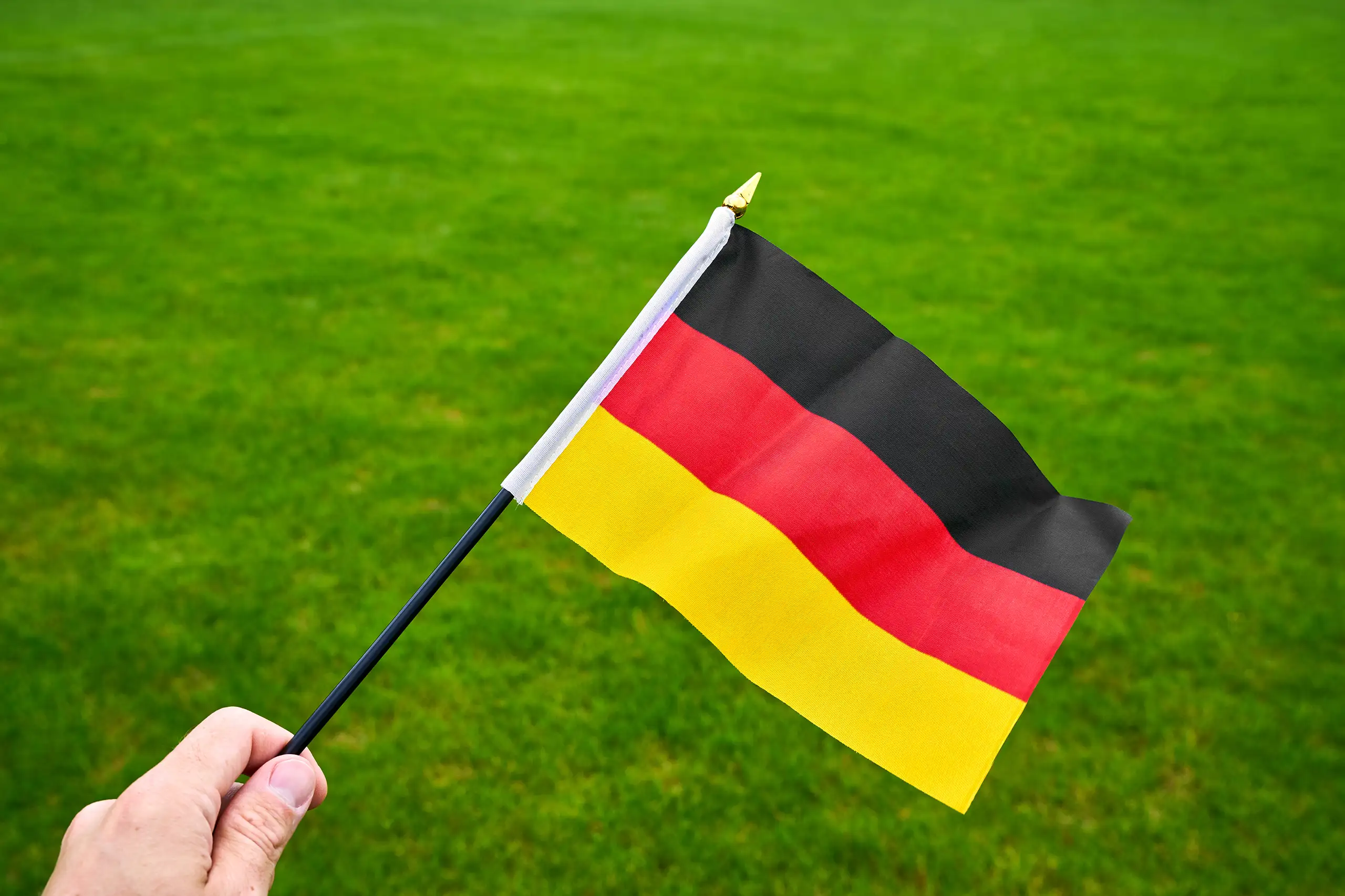 Deutschland-fahne wird von einer hand gehalten und weht vor einem grünen rasen im freien als symbol für deutschland und fußball.