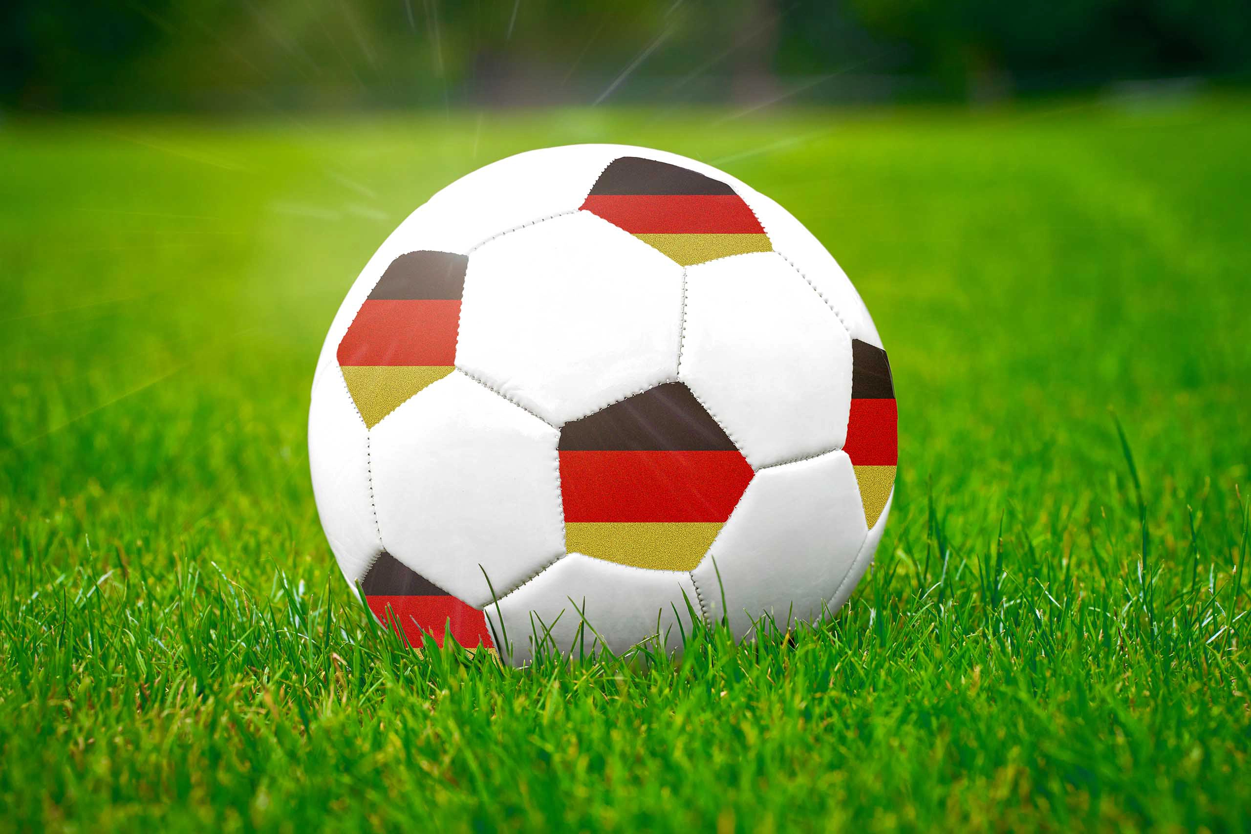 Deutschland fußballspiel mit fußball im design der deutschen nationalfarben auf grünem rasen.