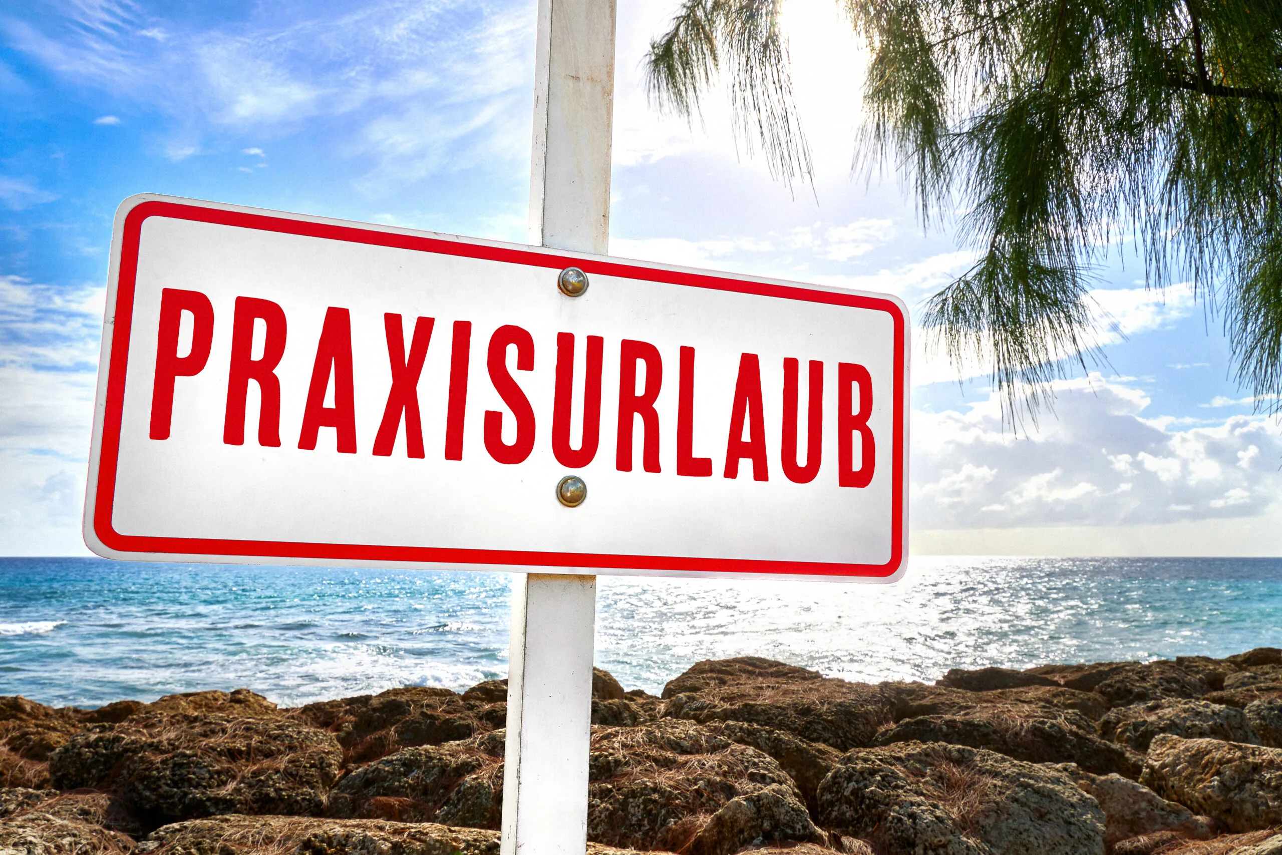 Schild mit der aufschrift praxisurlaub an einem sonnigen strand mit meer im hintergrund