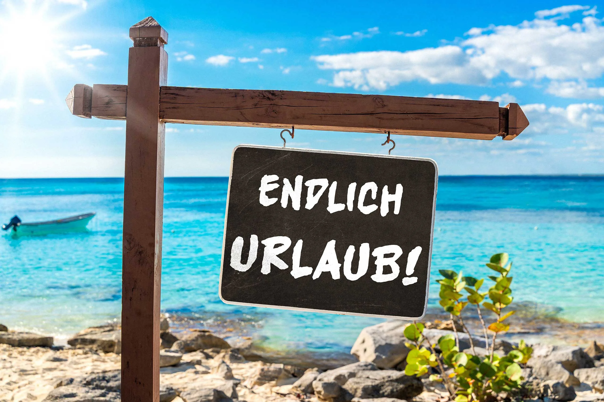 Holzschild mit der aufschrift endlich urlaub am sandigen strand vor blauem meer