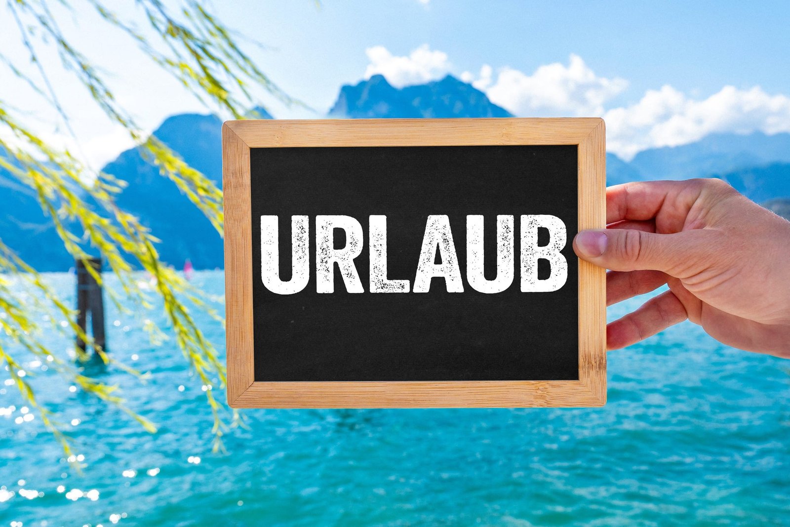 Hand hält eine schiefertafel mit der aufschrift urlaub vor einem see und bergen